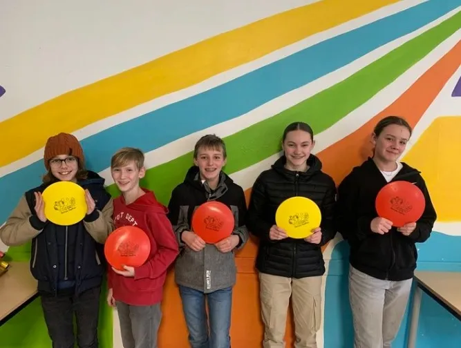 Groupe d'élèves souriants tenant des disques de sport colorés devant un mur rayé
